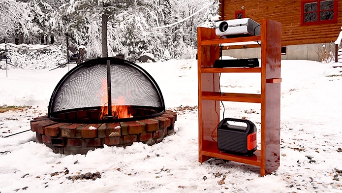 Timberline Custom Outdoor Projector Stand set up in the winter next to a burning bonfire.