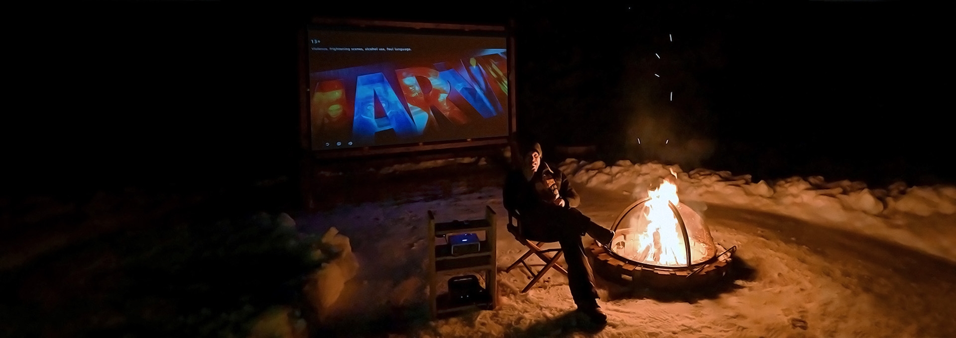 Todd Morton, founder of the Wireless Outdoor Cinema Company, sitting next to a bonfire in the winter.